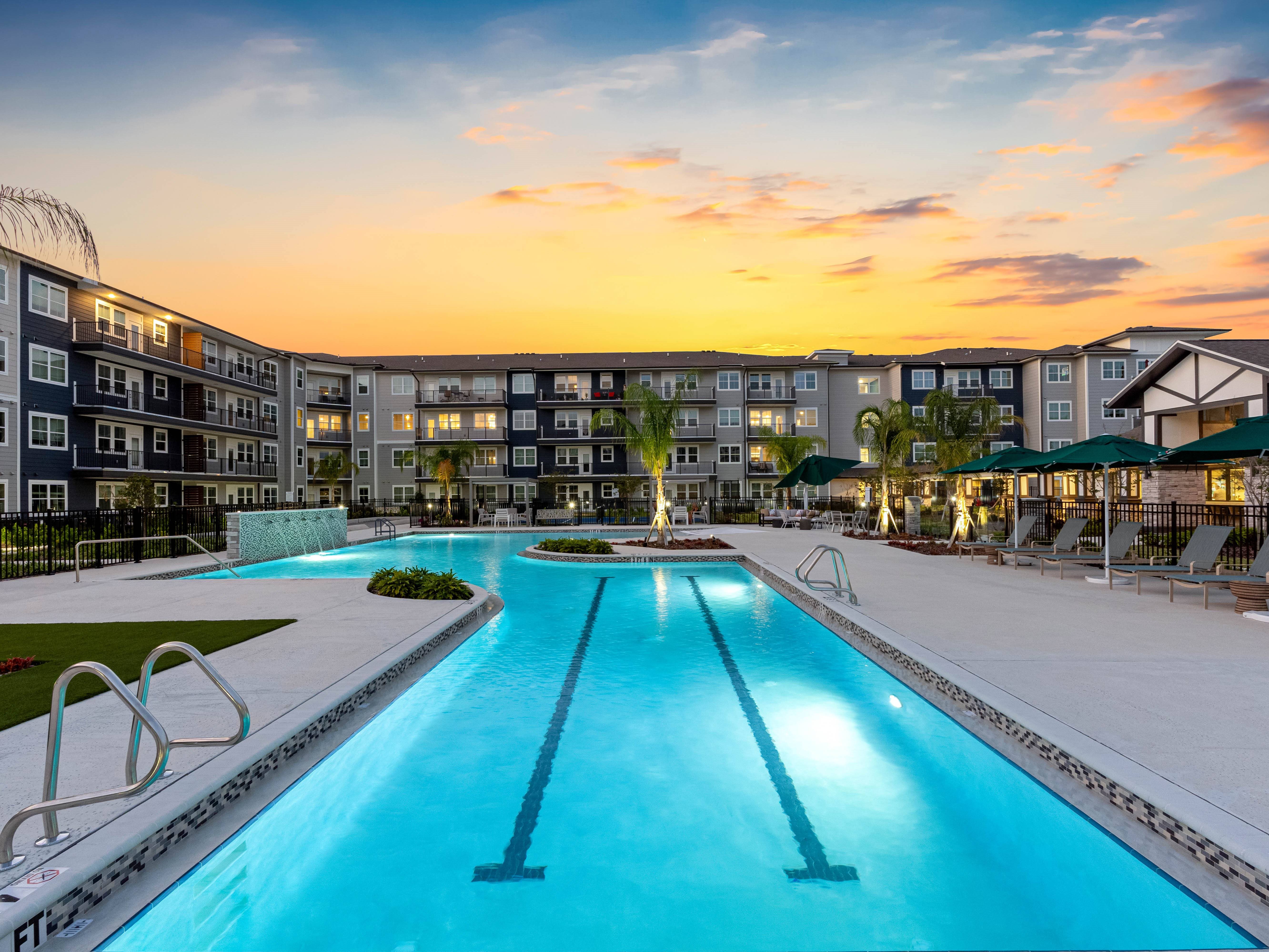 A large swimming pool in front of a building with a sunset in the background.